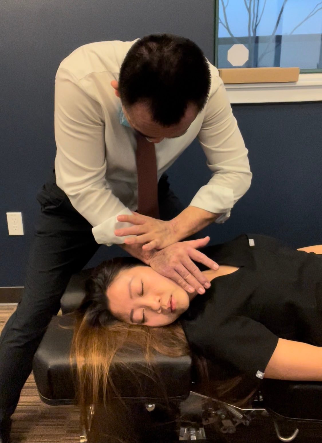 Chiropractor adjusting patient's neck and head on treatment table in office