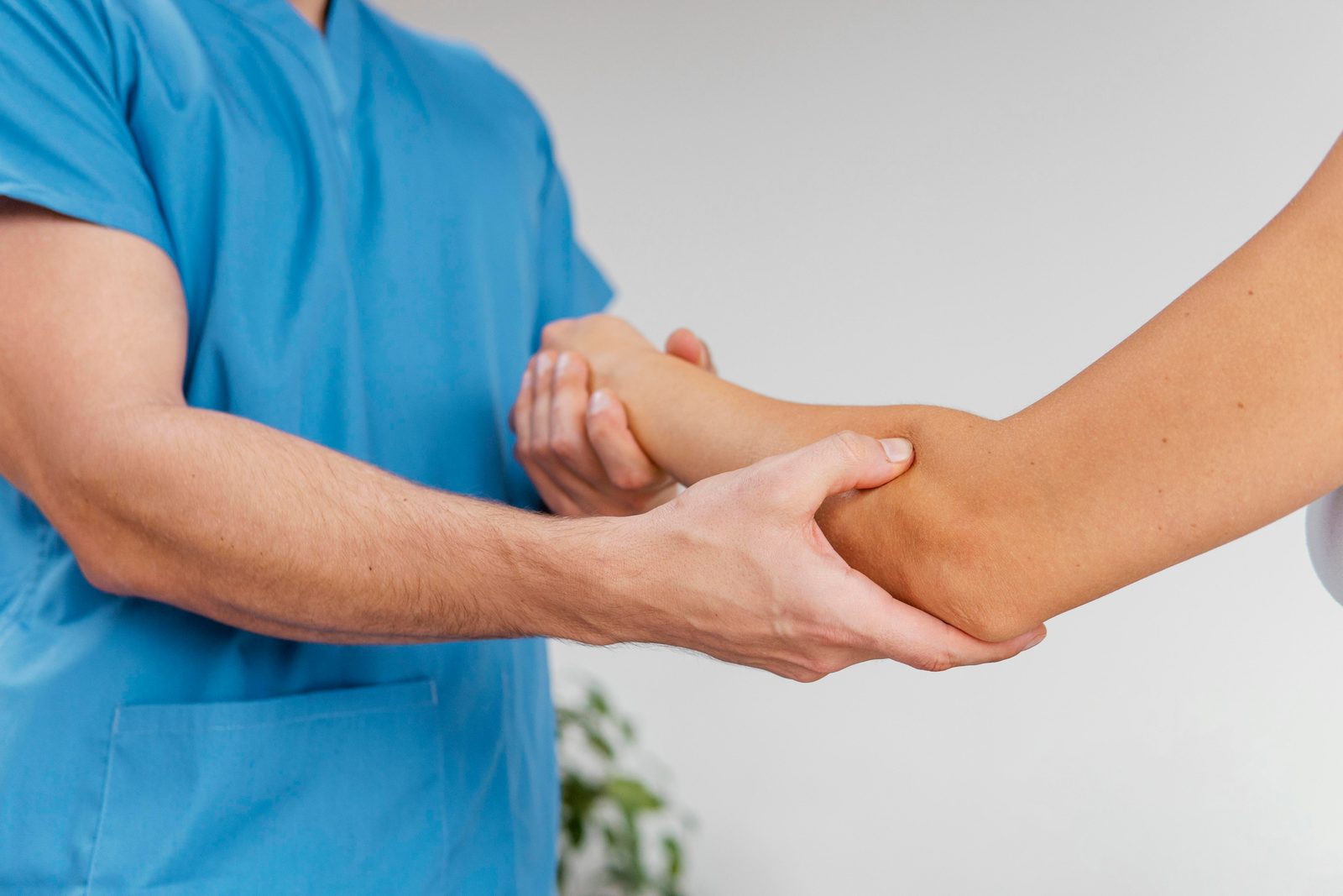 Healthcare provider in blue shirt examining patient's wrist and forearm with hands-on palpation